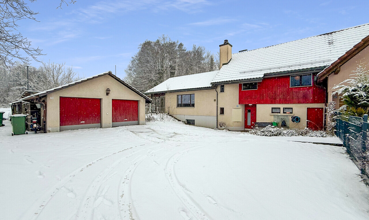 snow covered house featuring an outbuilding, a garage, and a chimney