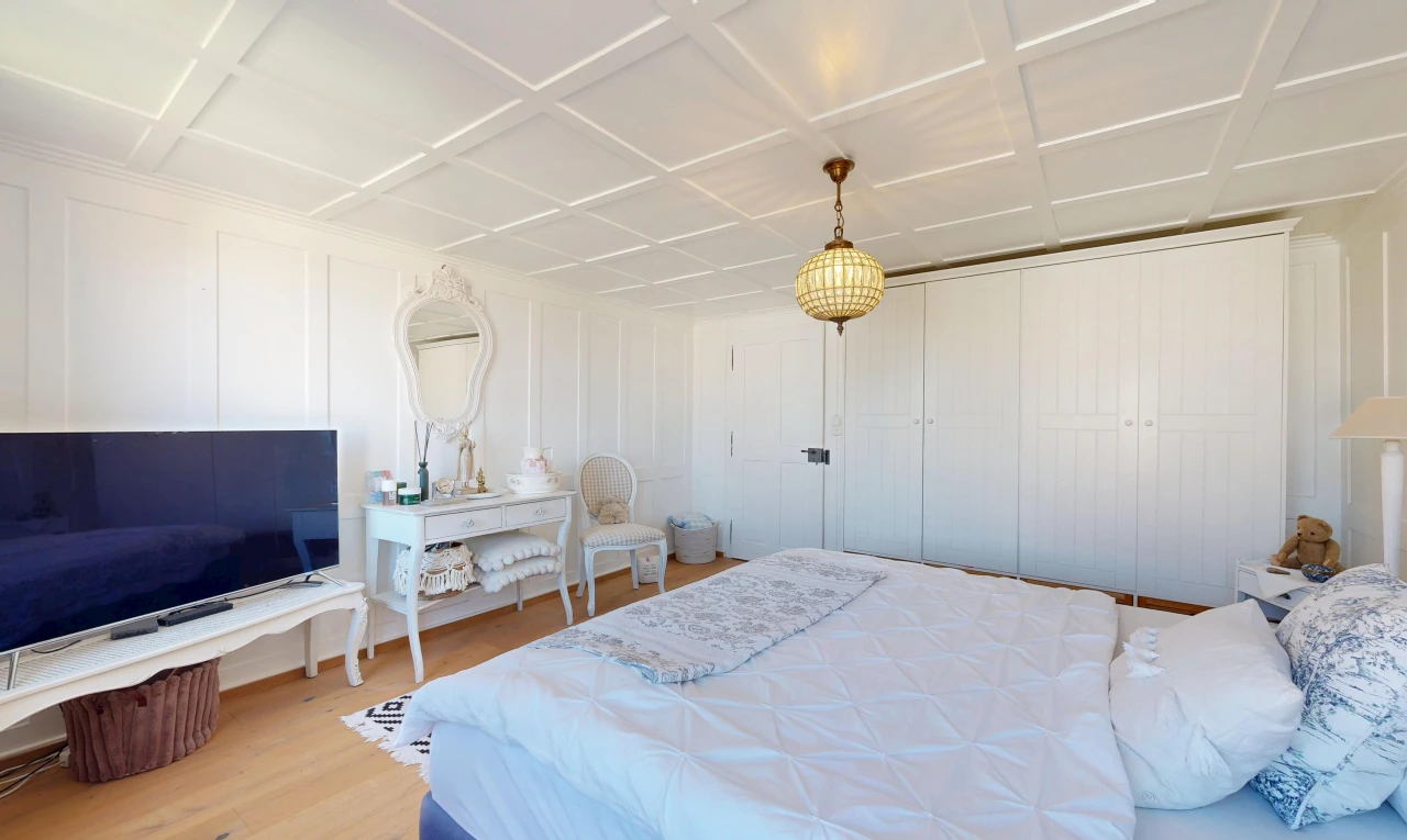 room / bedroom featuring light wood-style floors, coffered ceiling, hanging light fixtures, a decorative wall, and a closet
