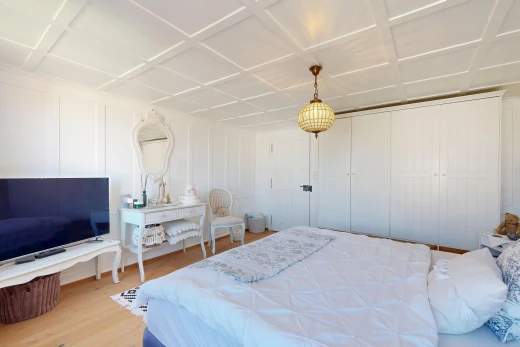 room / bedroom featuring light wood-style floors, coffered ceiling, hanging light fixtures, a decorative wall, and a closet
