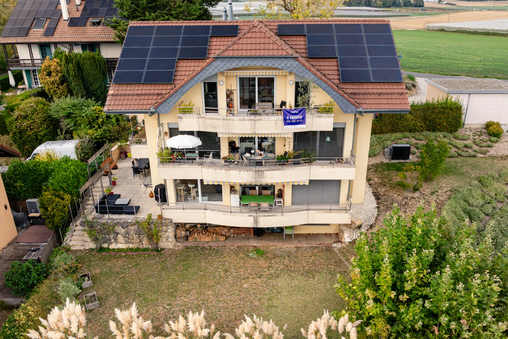 façade avec panneaux solaires, coin repas extérieur, toit en tuiles, property visible, et drone view
