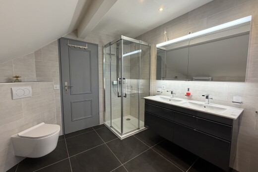 full bath featuring tile walls, double vanity, a stall shower, lofted ceiling with beams, and dark tile patterned floors