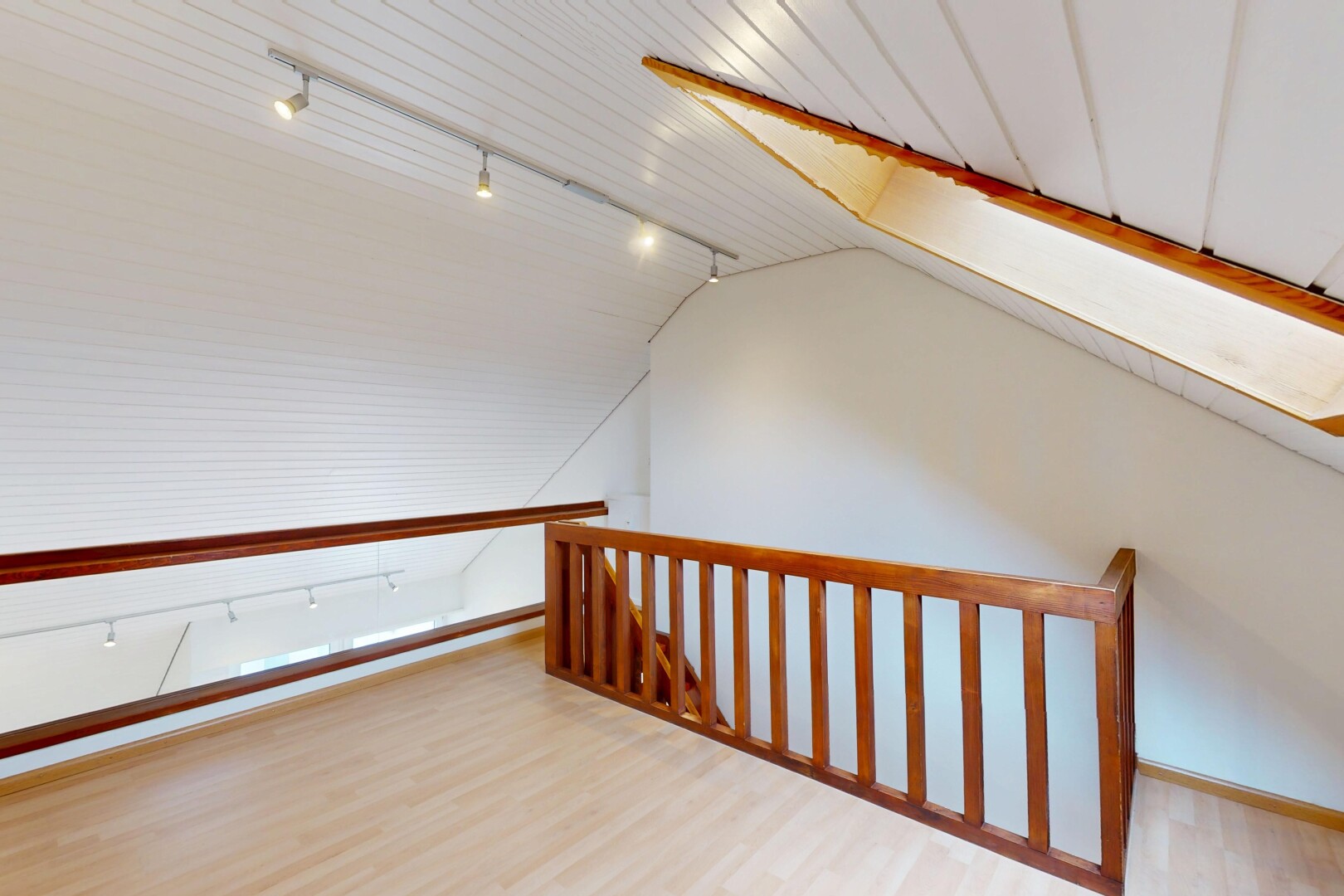 espace intérieur avec sol en finition bois, éclairage sur rail, plafond voûté, cloison sèche, et plinthes murales