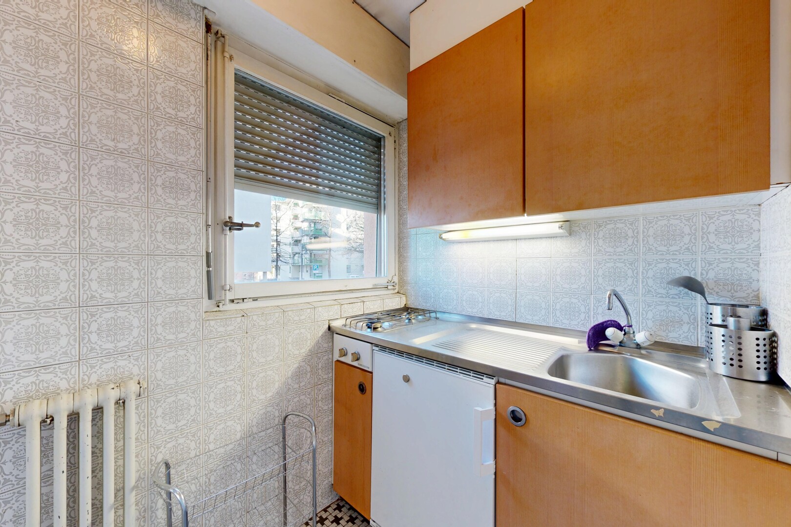 kitchen with stainless steel countertops, brown cabinetry, dishwasher, and radiator heating unit