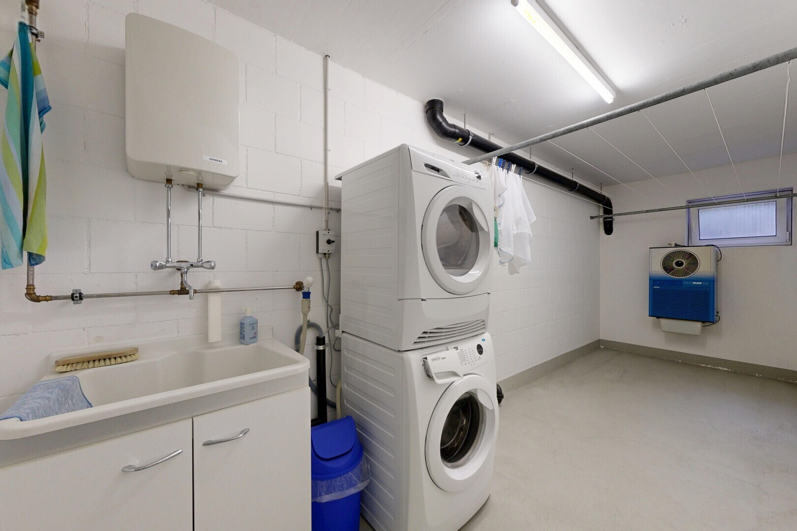 wäschekammer mit wasserkocher, waschturm, waschbecken, inside property, und betonboden