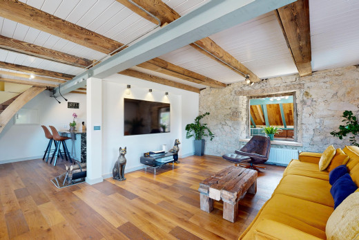 wohnzimmer mit parkettboden, fernseher, balkendecke, kühler, und steinwand