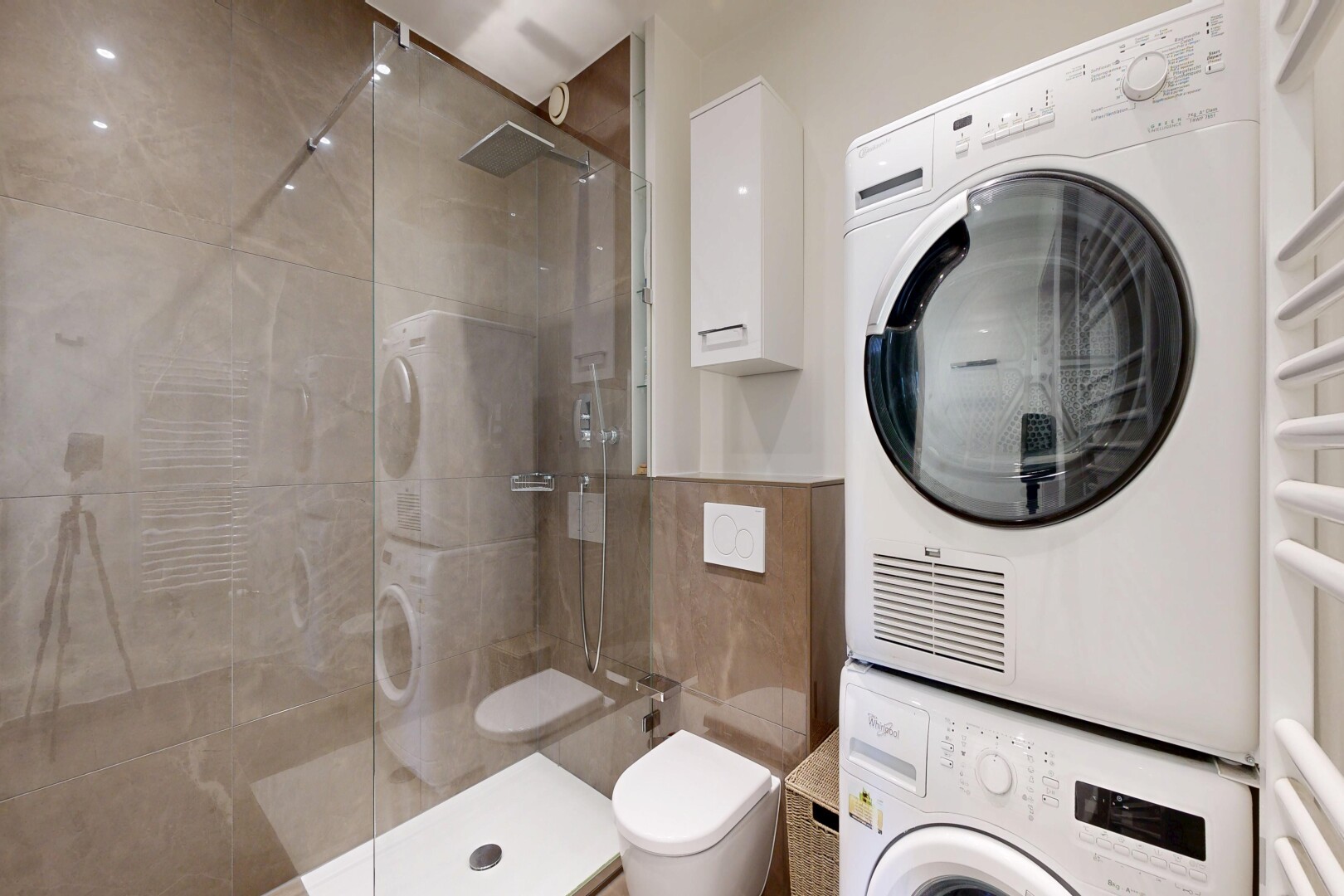 full bath featuring stacked washer and dryer, a shower stall, a towel warmer, and tile walls