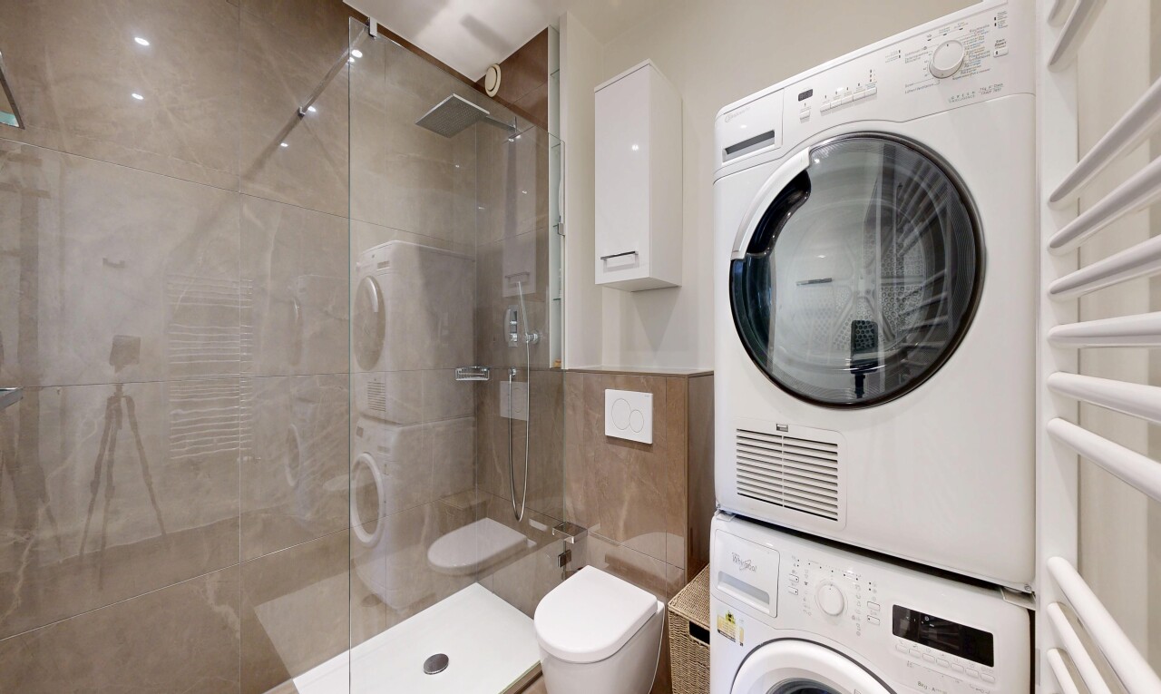 full bath featuring stacked washer and dryer, a shower stall, a towel warmer, and tile walls