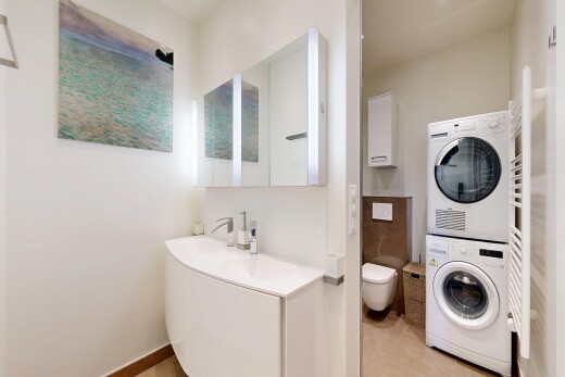 salle de bains avec chauffe-serviettes, miroir, lave-linge et sèche-linge superposés, lavabo (ou coiffeuse selon le contexte), et cloison sèche