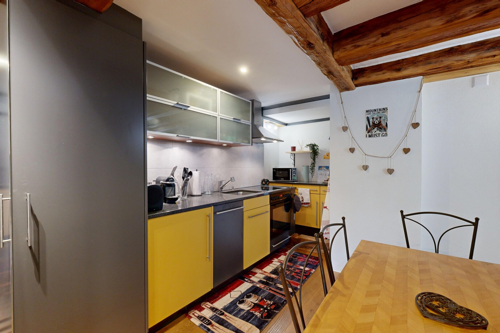 cuisine avec dark countertops, hotte, beamed ceiling, plafond à poutres, et armoires avec insert en verre