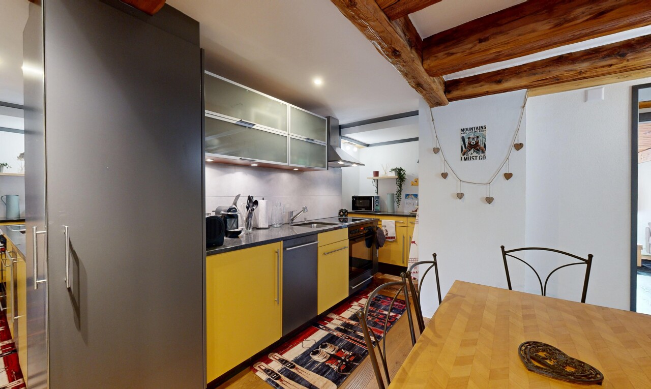 cuisine avec dark countertops, hotte, beamed ceiling, plafond à poutres, et armoires avec insert en verre