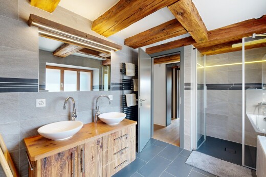 full bathroom featuring tile walls, double vanity, a stall shower, beamed ceiling, and dark tile patterned floors