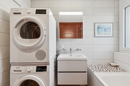 buanderie avec lave-linge et sèche-linge superposés, évier, inside property, tile wall, et mur en carrelage