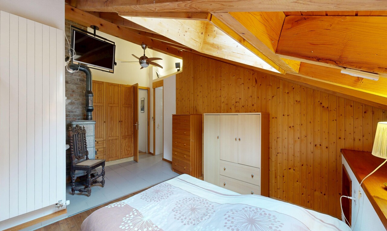 zimmer / schlafzimmer mit holzofen, dachschräge, vaulted ceiling, fernseher, und holzwand
