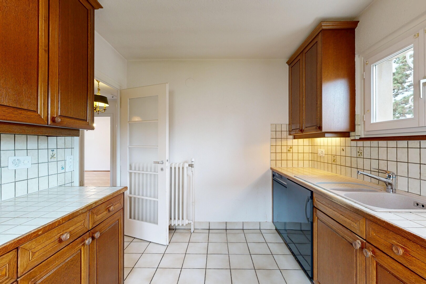 kitchen featuring tasteful backsplash, tile counters, wood finish cabinetry, black dishwasher, and radiator