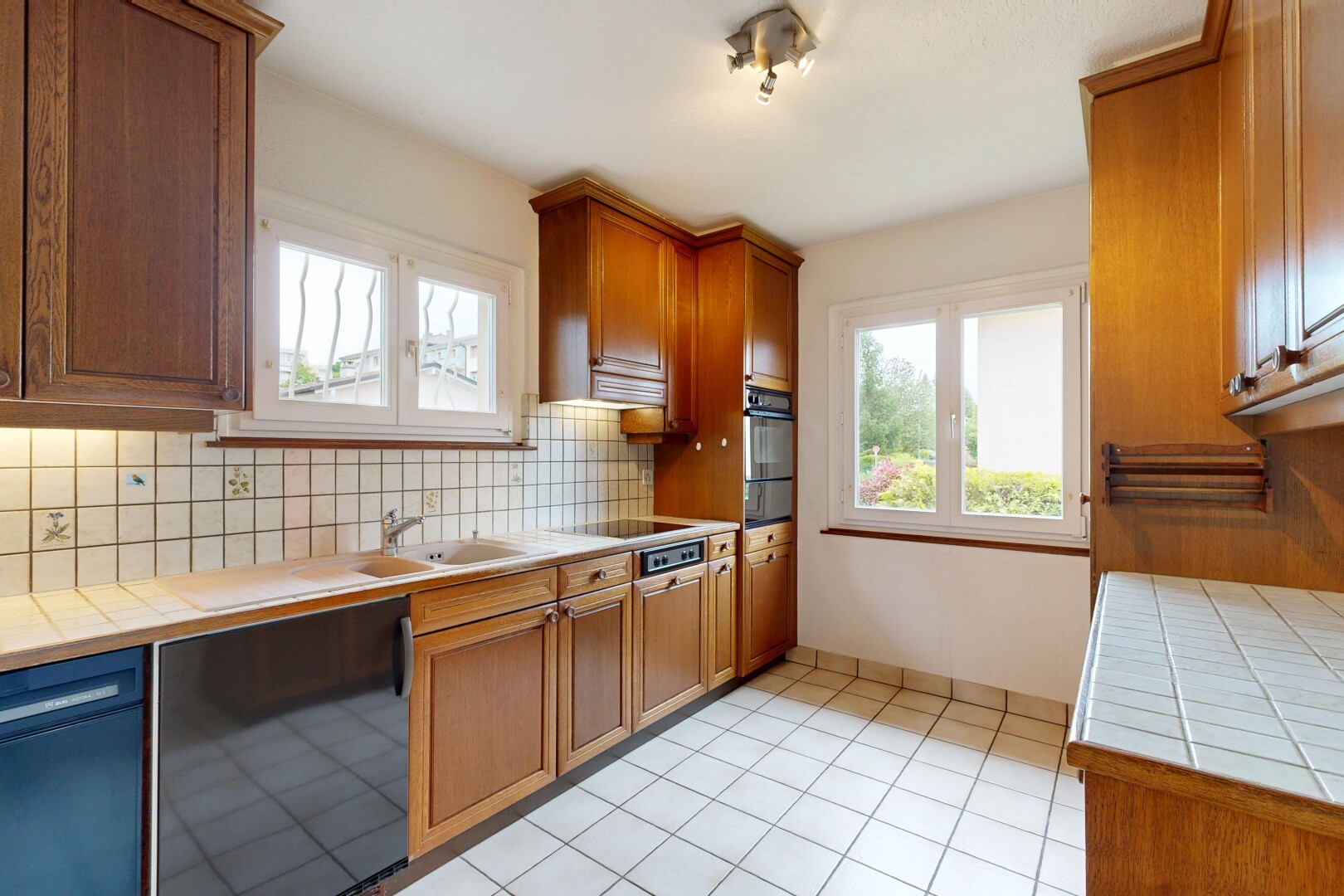 kitchen featuring tile countertops, black dishwasher, wood finish cabinetry, wall oven, and decorative backsplash