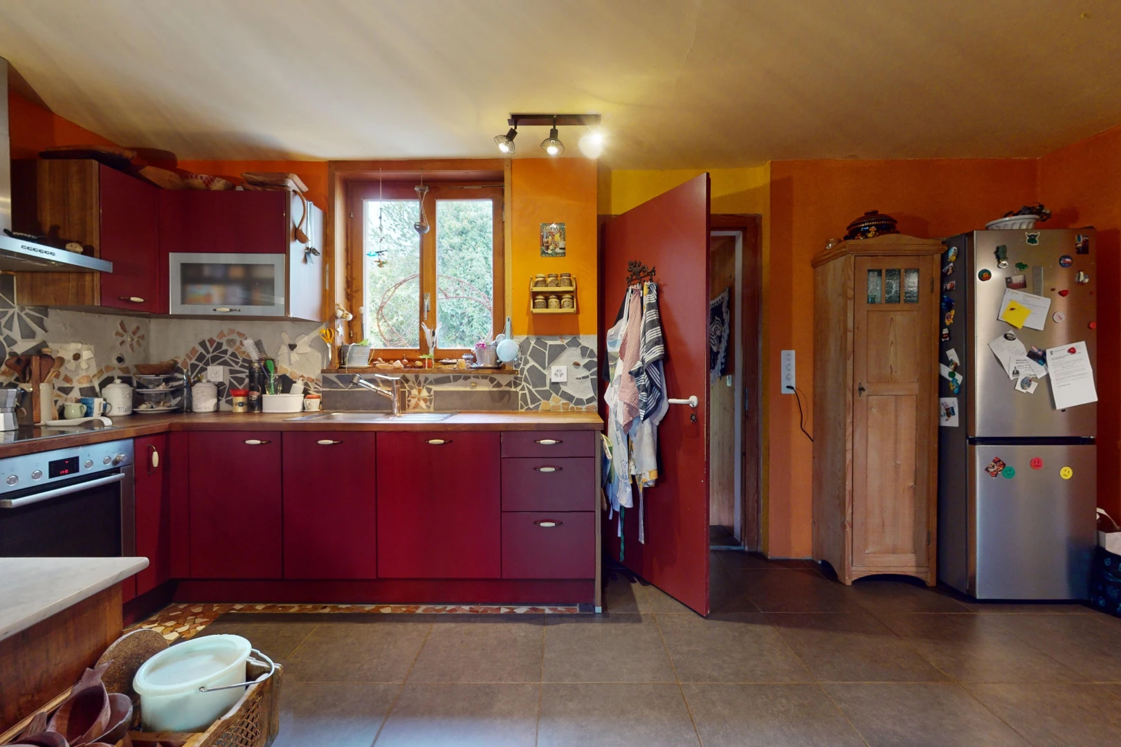 cuisine avec crédence, four, lumière naturelle, meubles rouges, et réfrigérateur