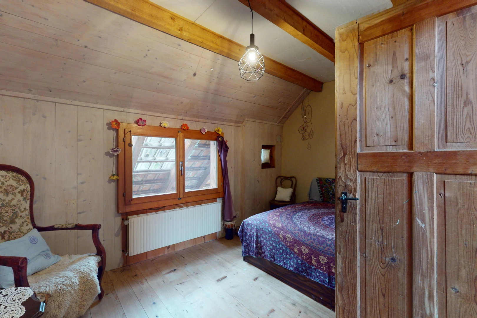 chambre avec plancher de bois, poutres apparentes, lumière naturelle, plafond voûté, et radiateur