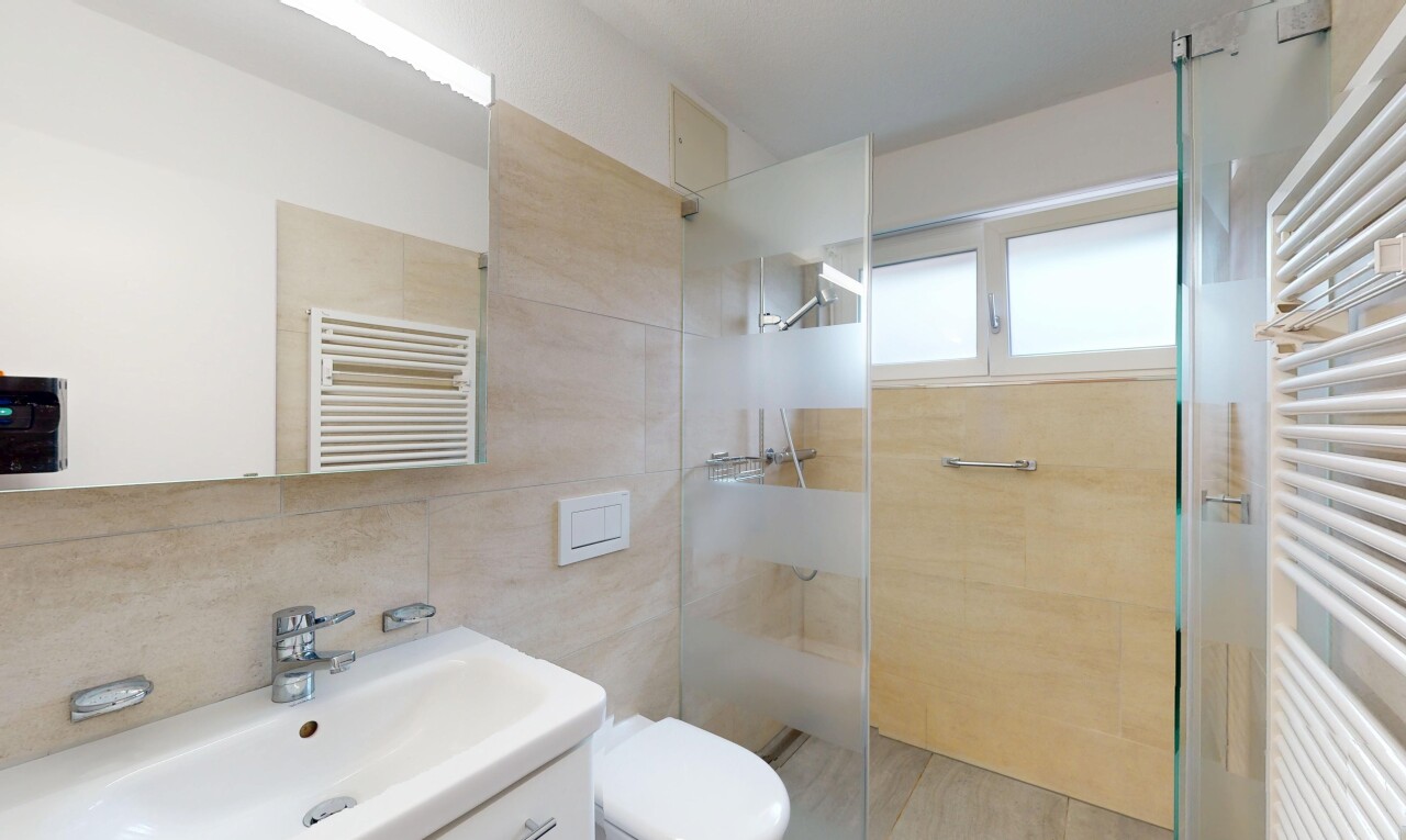 bathroom featuring a towel warmer, radiator, tiled shower, vanity, and tile walls
