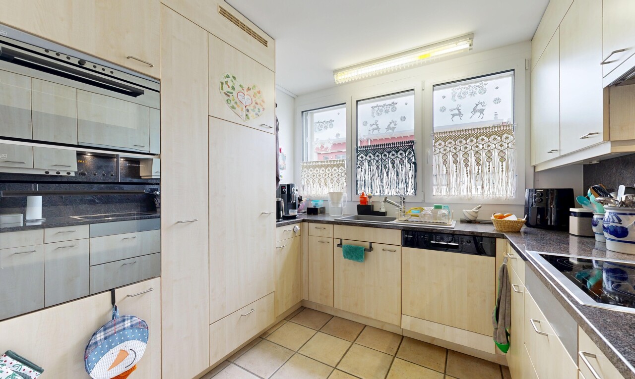 kitchen featuring dark countertops, black appliances, light tile patterned floors, and light wood finish cabinetry