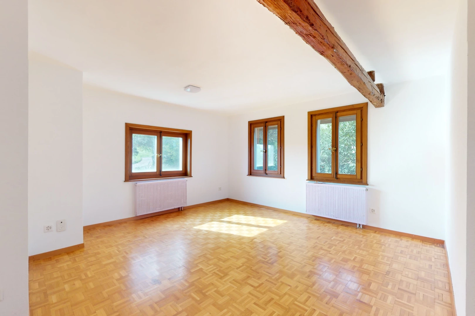 pièce vide avec poutres apparentes, lumière naturelle, radiateur, et parquet