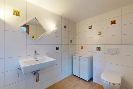 salle de bain avec mur carrelé, miroir, vasque, plancher de bois, et toilettes