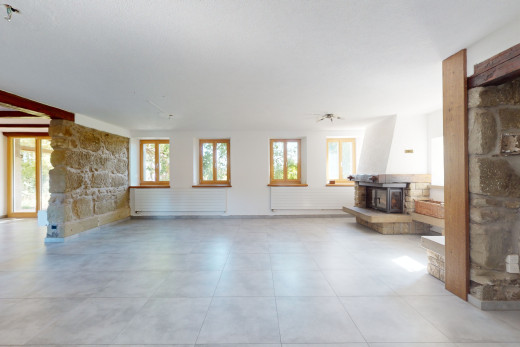 salon avec lumière naturelle, carrelage, poêle à bois, et mur en pierre