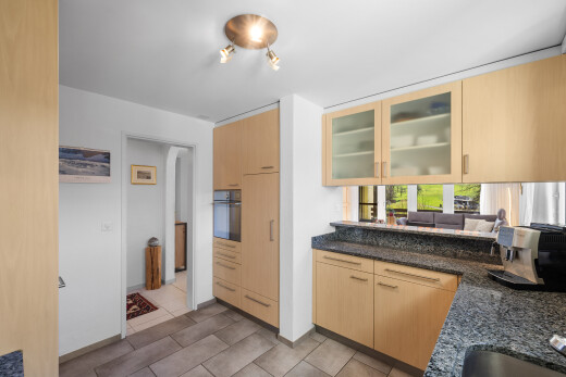 küche mit two heights countertops, dark countertops, schränke mit glastüren, glass insert cabinets, und hellbraune schränke