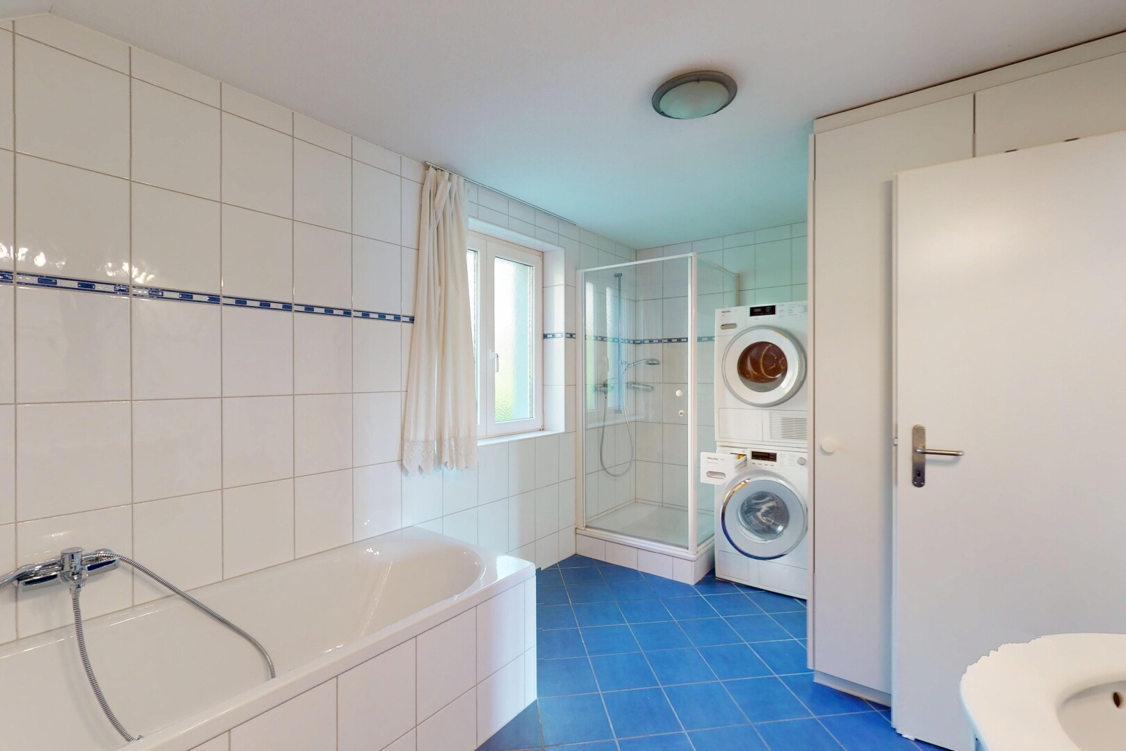 salle de bains avec douche, lave-linge et sèche-linge superposés, bain, sol en carrelage, et lumière naturelle