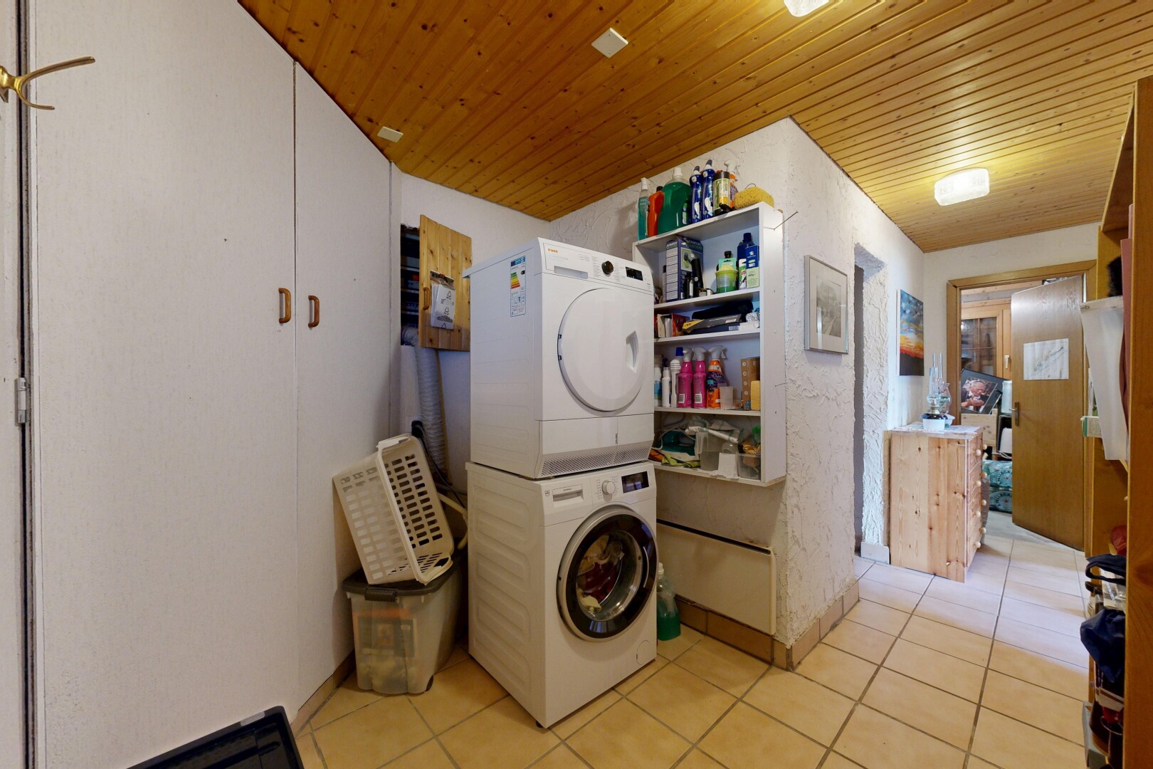 laundry area featuring light tile patterned floors, stacked washer and clothes dryer, and wood ceiling