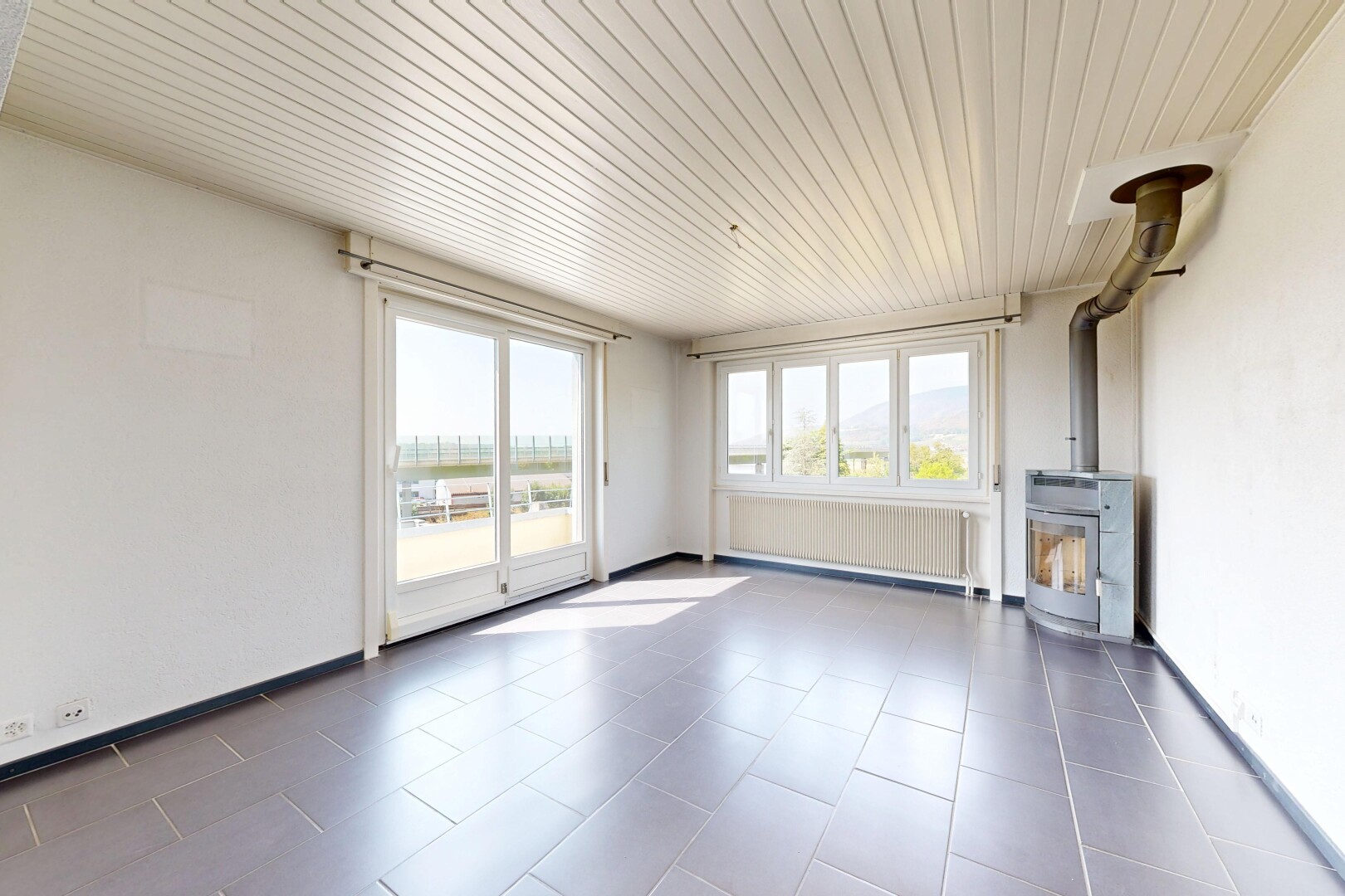 pièce vide avec poêle à bois, radiateur, cloison sèche, drywall, et plafond en bois