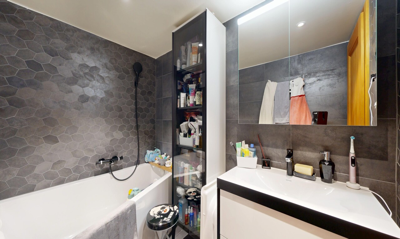 salle de bains avec mur en carrelage, tile wall, lavabo (ou coiffeuse selon le contexte), miroir, et salle de bain complète