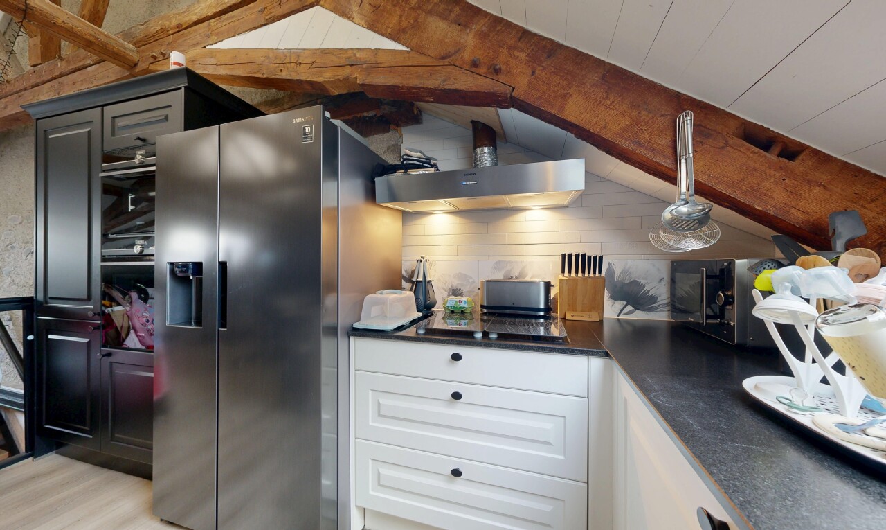 cuisine avec dark countertops, beamed ceiling, plafond à poutres, hotte, et armoires élevées