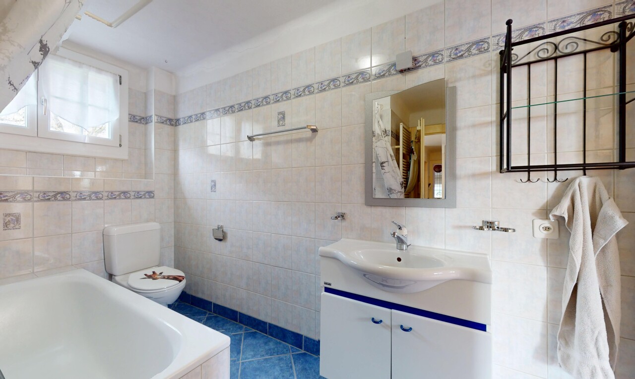 salle de bains avec mur carrelé, vasque, meuble-lavabo, toilettes, et miroir