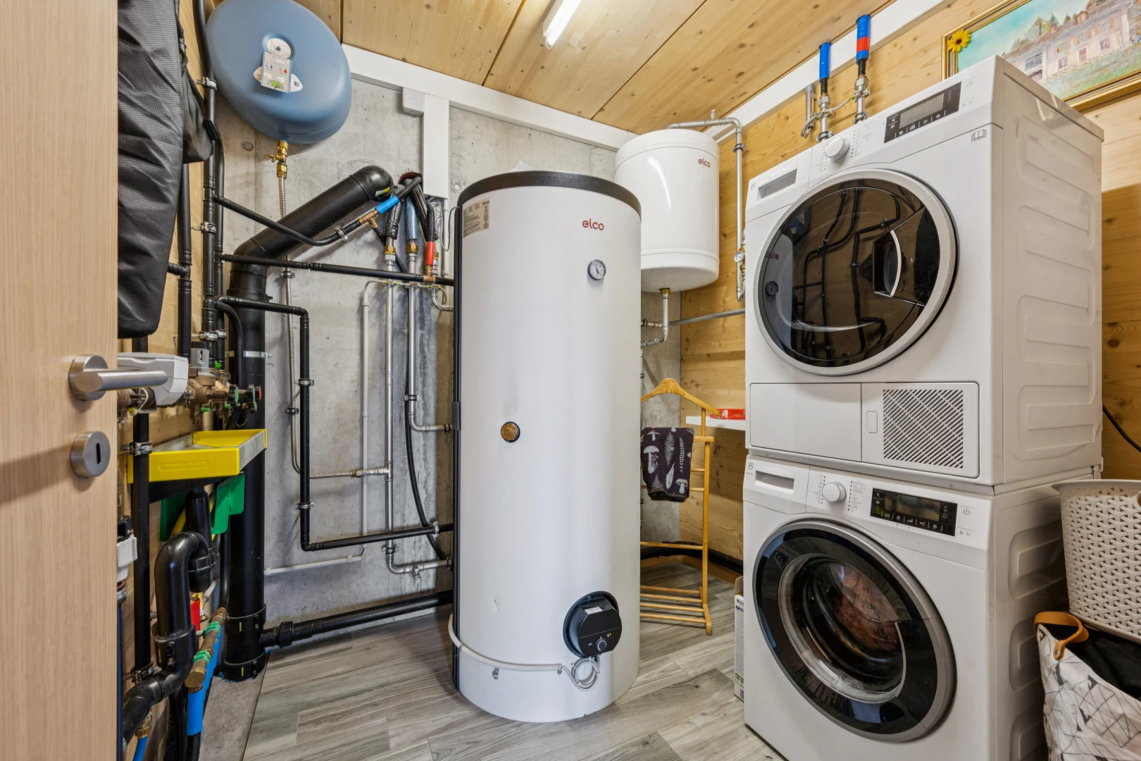 buanderie avec chauffe-eau, lave-linge et sèche-linge superposés, réservoir d'expansion d'eau, buanderie, et wood finish floor