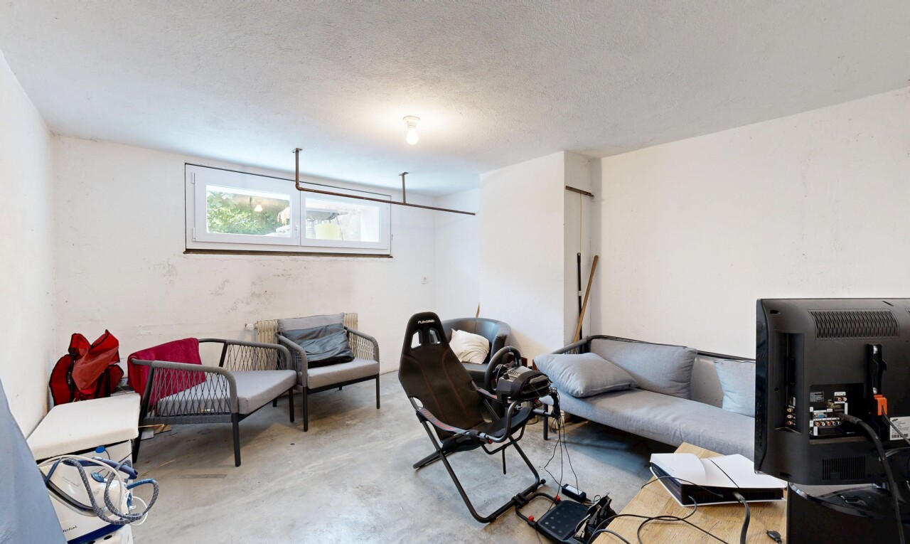salon avec sol en béton, concrete floor, sous-sol, télévision, et lumière naturelle