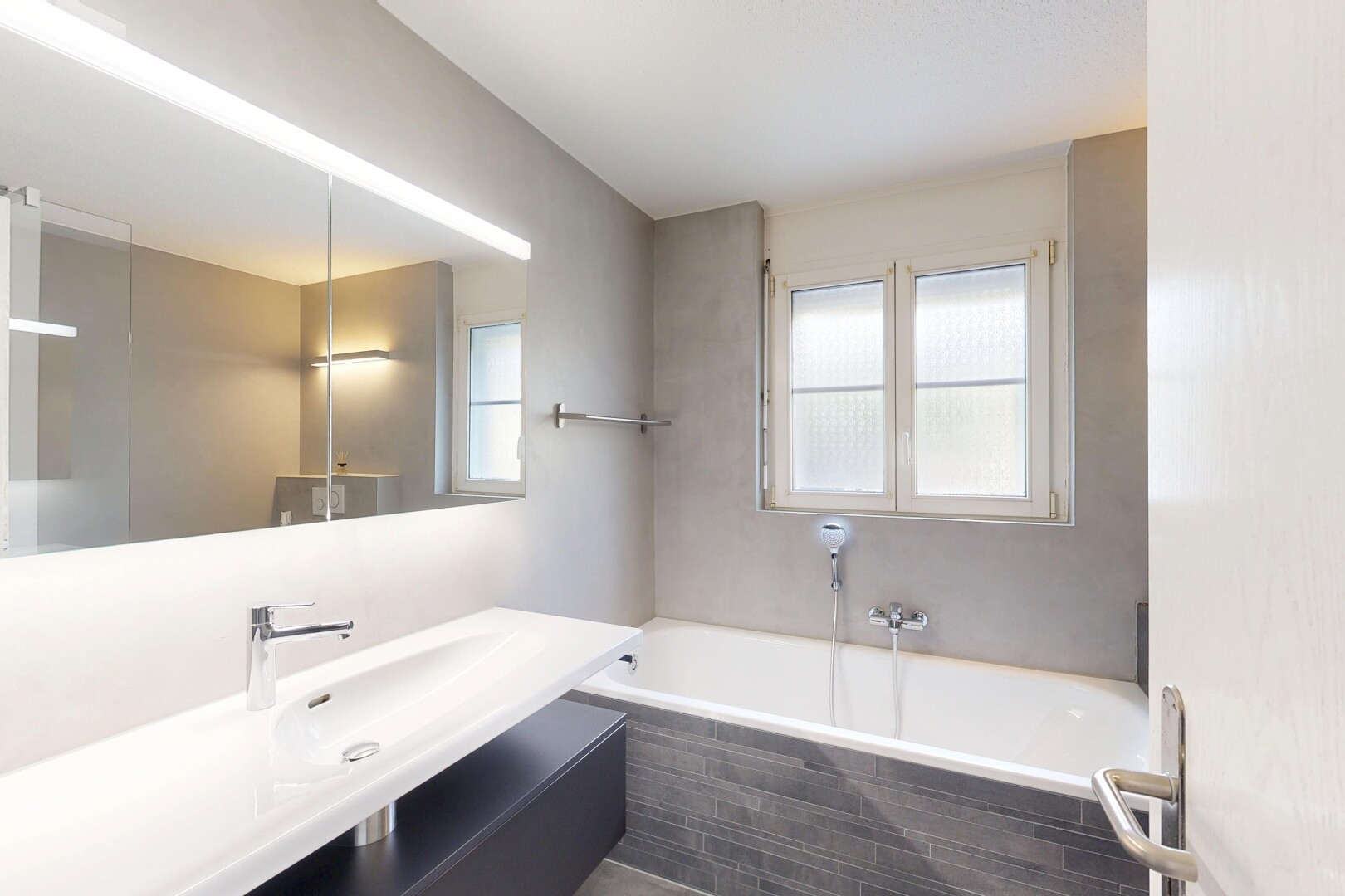 salle de bains avec salle de bain complète, miroir, lavabo (ou coiffeuse selon le contexte), bain, et lumière naturelle
