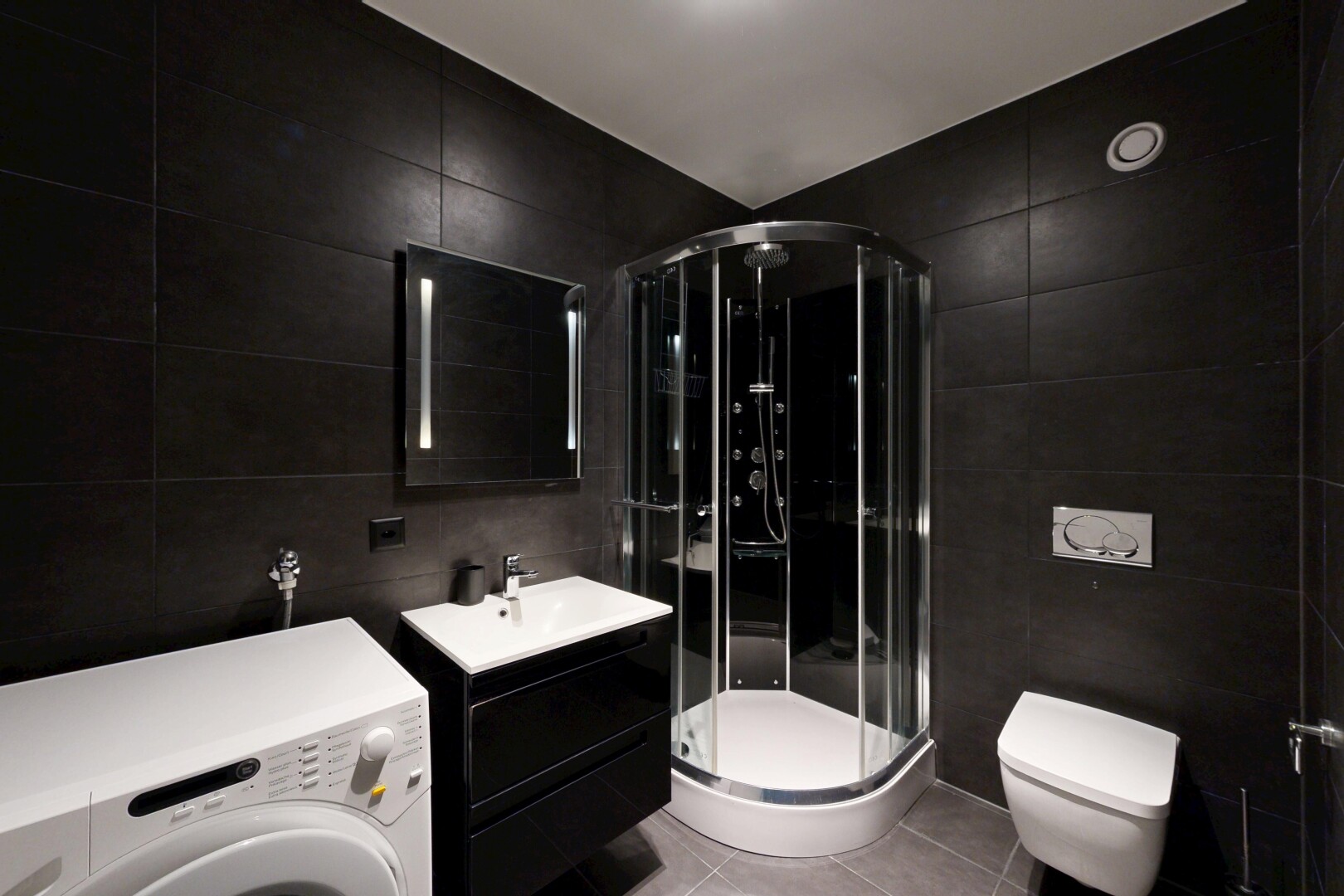salle de bains avec tile wall, mur en carrelage, lave-linge et sèche-linge, lavabo (ou coiffeuse selon le contexte), et light floor