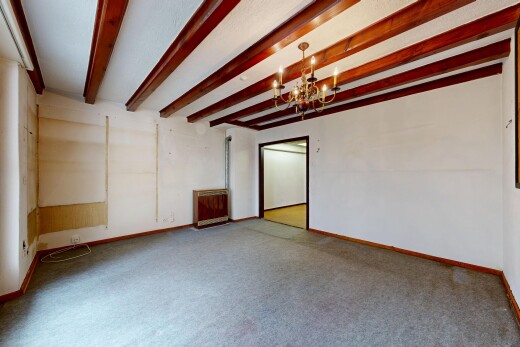 carpeted empty room with hanging lights and beam ceiling