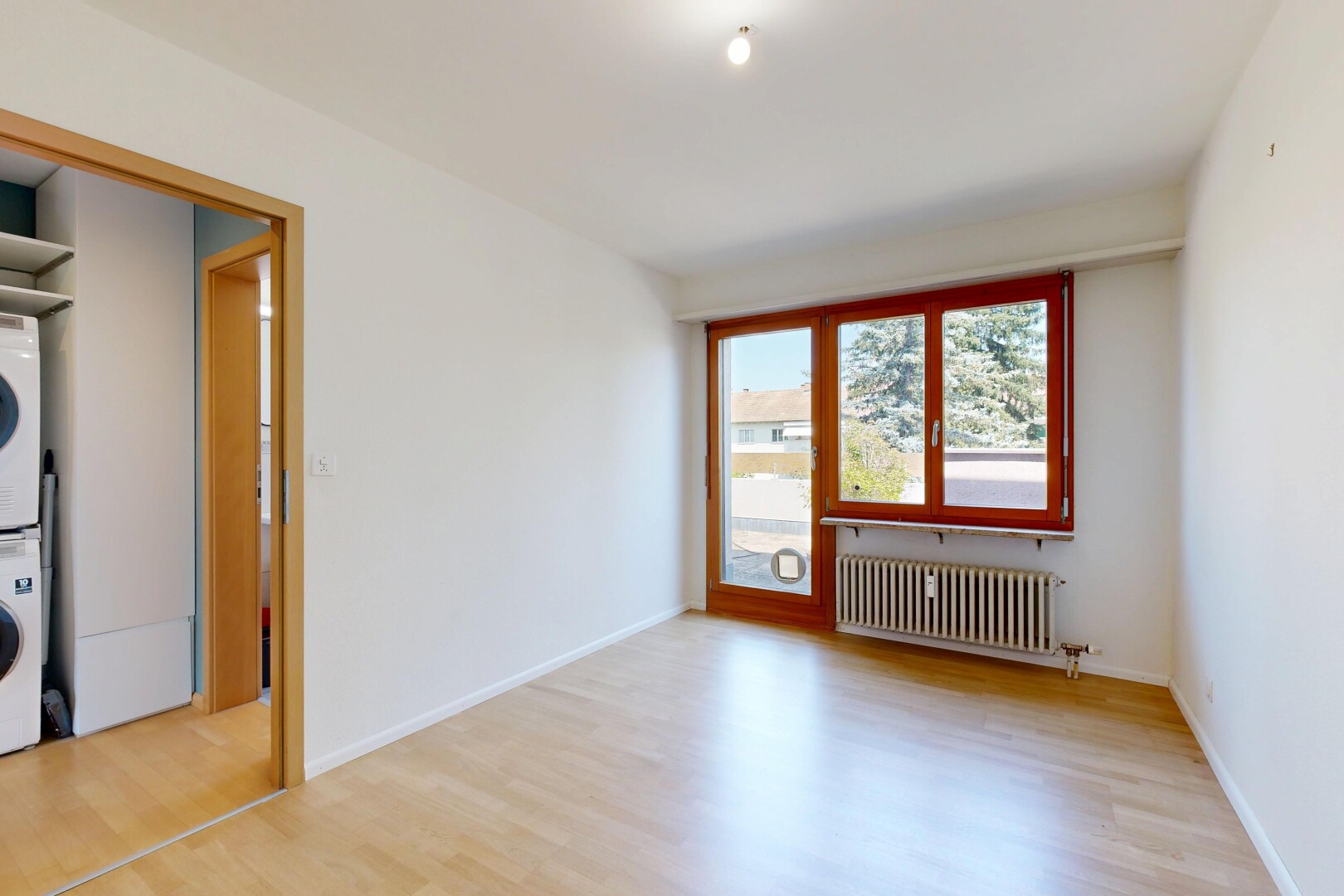 pièce vide avec wood finish floor, sol en finition bois, lave-linge et sèche-linge superposés, inside property, et radiateur