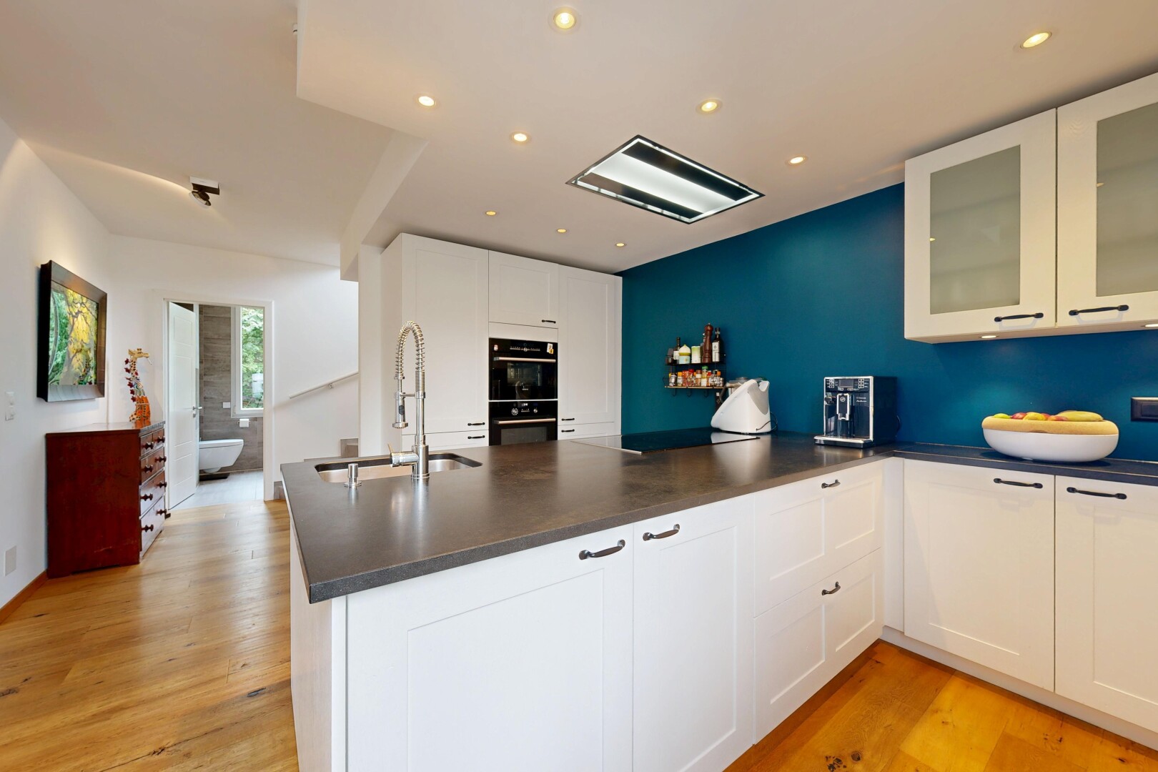 cuisine avec sol en finition bois, wood finish floor, armoires avec insert en verre, plans de travail, et lumière naturelle