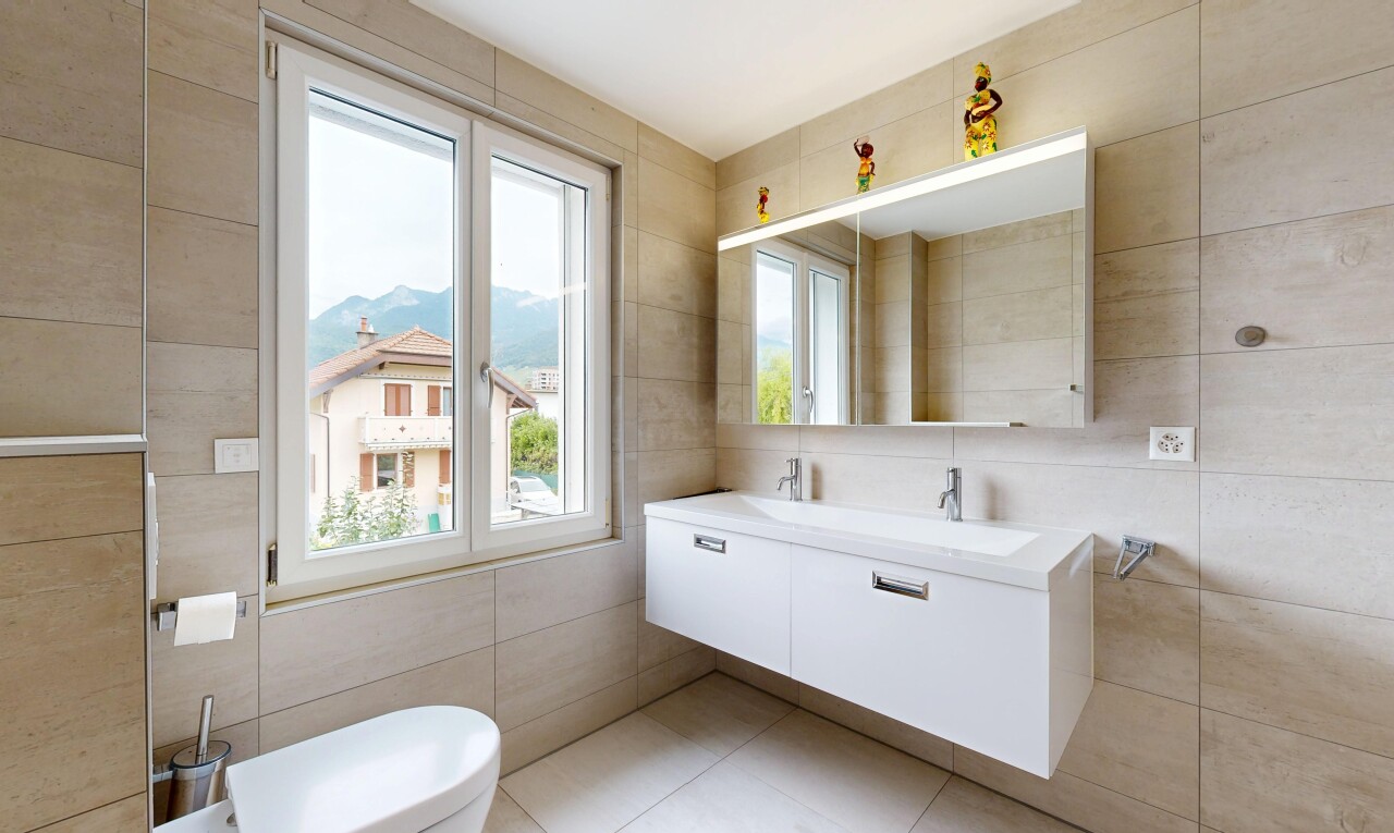 salle de bains avec mur en carrelage, tile wall, miroir, toilette, et lumière naturelle