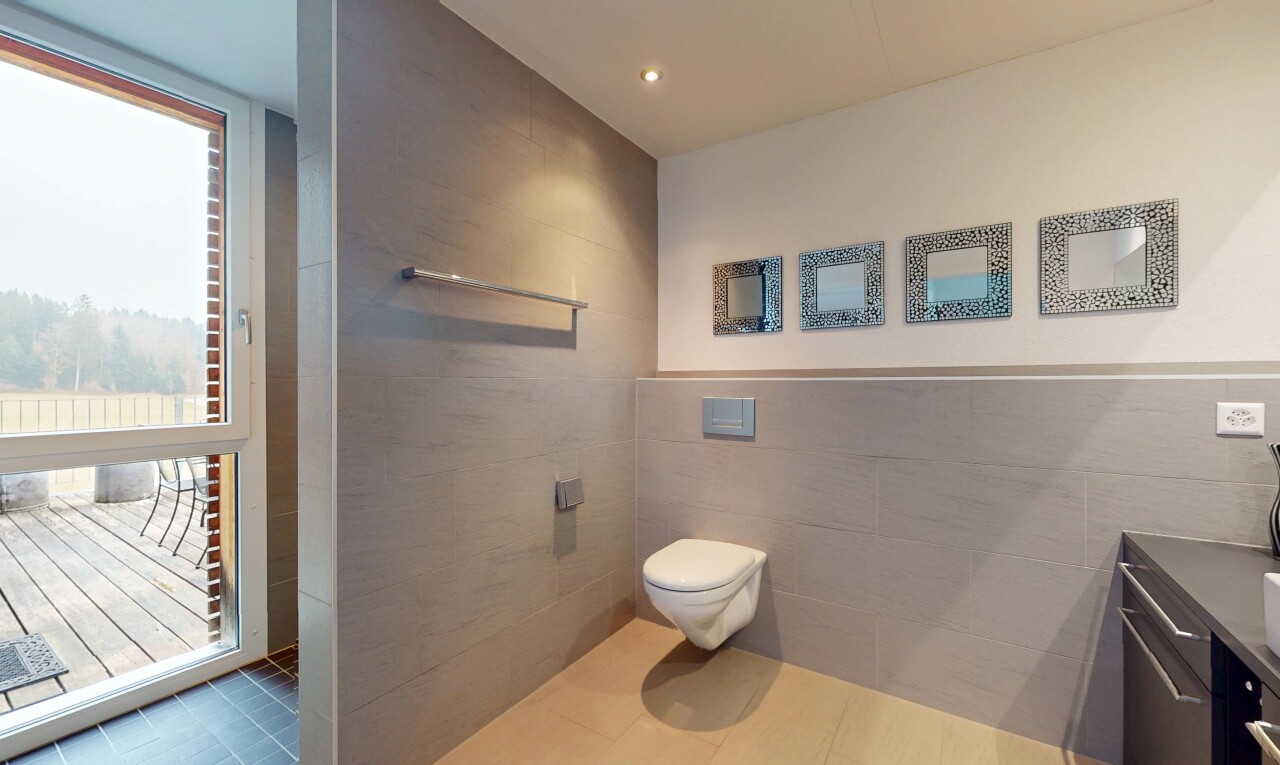 salle de bains avec toilettes, meuble-lavabo, lumière naturelle, carrelage, et mur carrelé