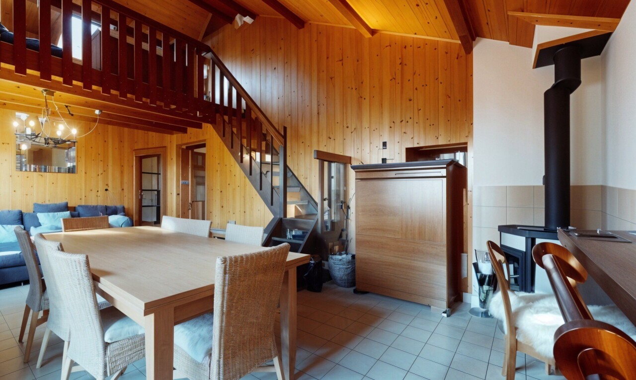 salle à manger avec lustre, poêle à bois, poutres apparentes, mur en bois, et carrelage