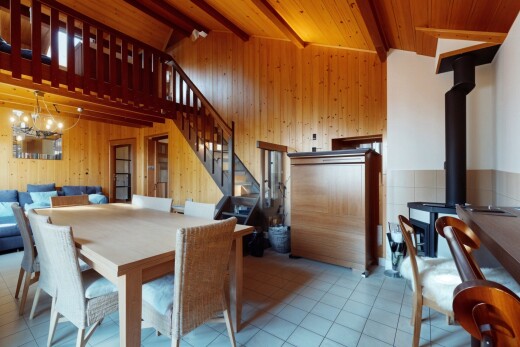salle à manger avec lustre, poêle à bois, poutres apparentes, mur en bois, et carrelage