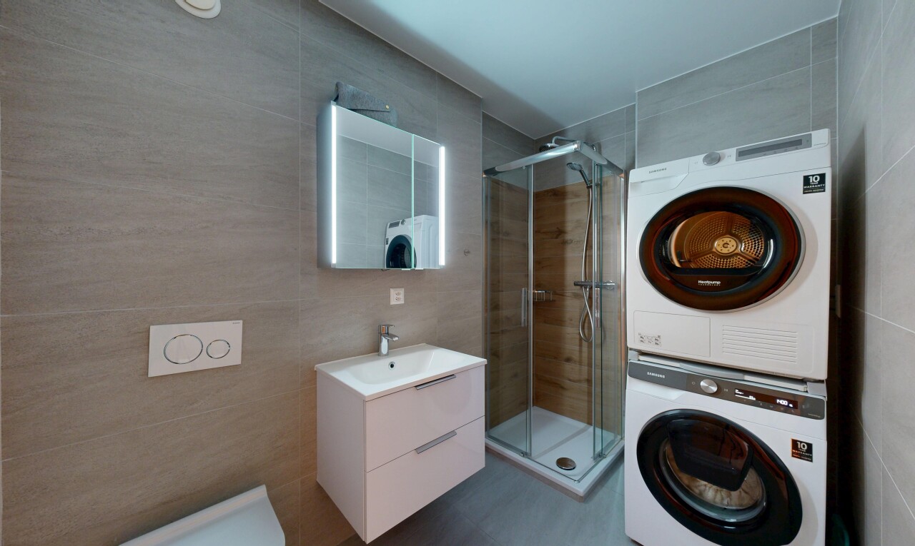bathroom featuring tile walls, a stall shower, stacked washing machine and dryer, and vanity