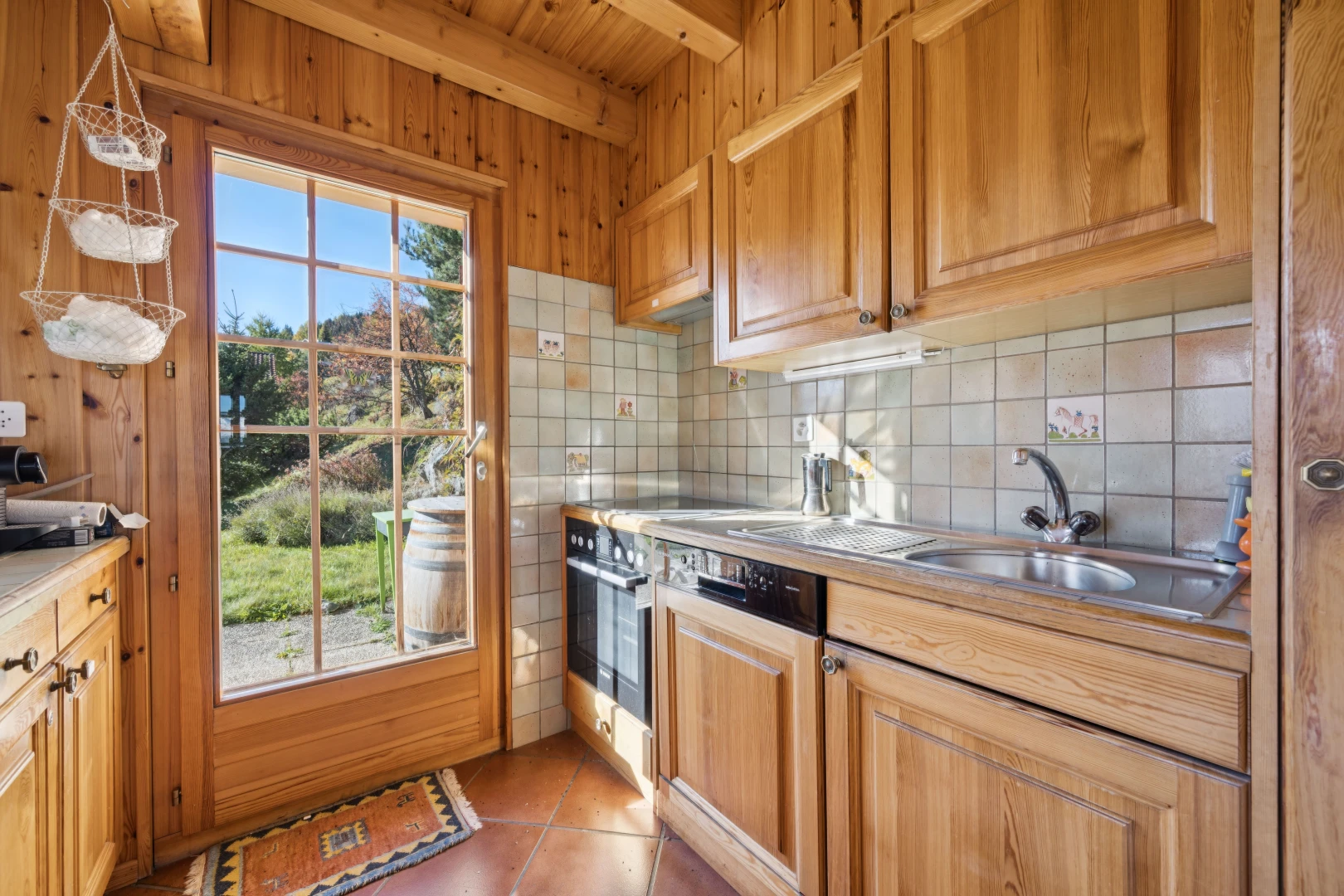 kitchen featuring backsplash, light tile patterned flooring, light countertops, wood finish cabinetry, and beamed ceiling