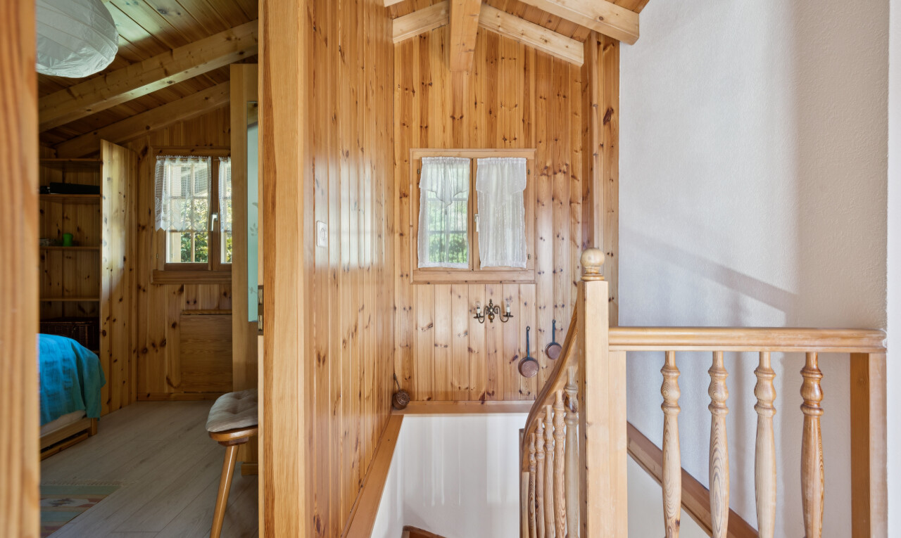 corridor with an upstairs landing, lofted ceiling with beams, wooden walls, wood finished floors, and wood ceiling