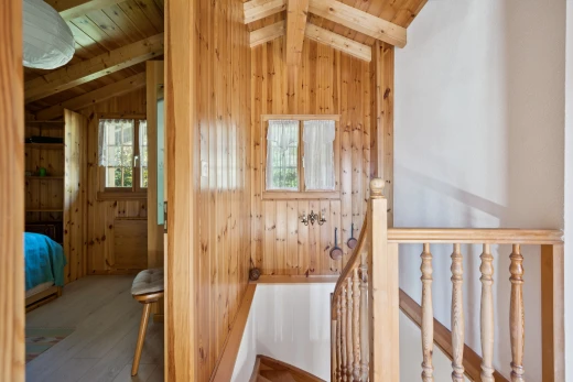 corridor with an upstairs landing, lofted ceiling with beams, wooden walls, wood finished floors, and wood ceiling