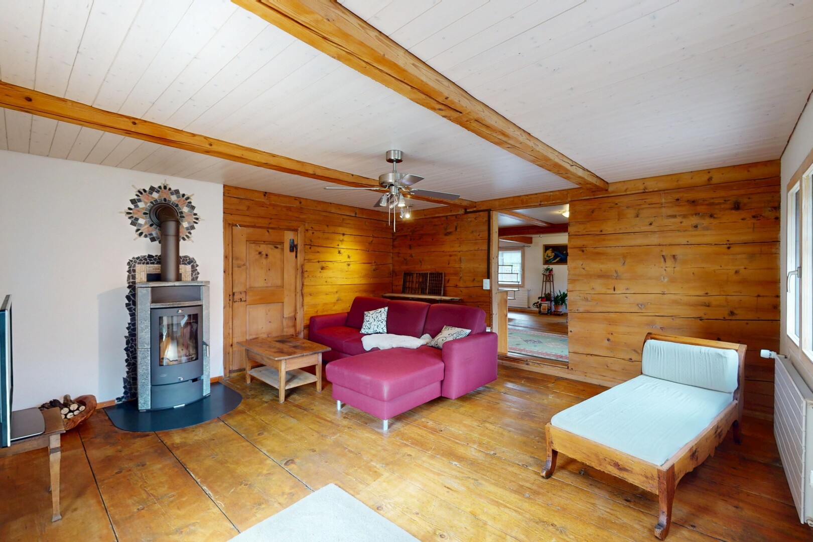 salon avec lumière naturelle, plafond à poutres, poêle à bois, et mur en bois