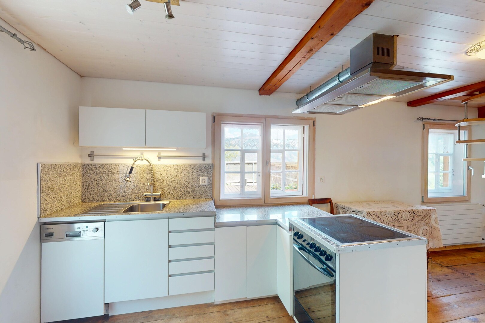 cuisine avec lave-vaisselle, lumière naturelle, plans de travail, sol en finition bois, et dosseret